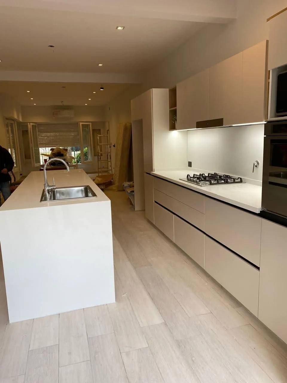 Cocina con muebles claros, mesadas blancas, isla y anafe, durante la etapa de terminación