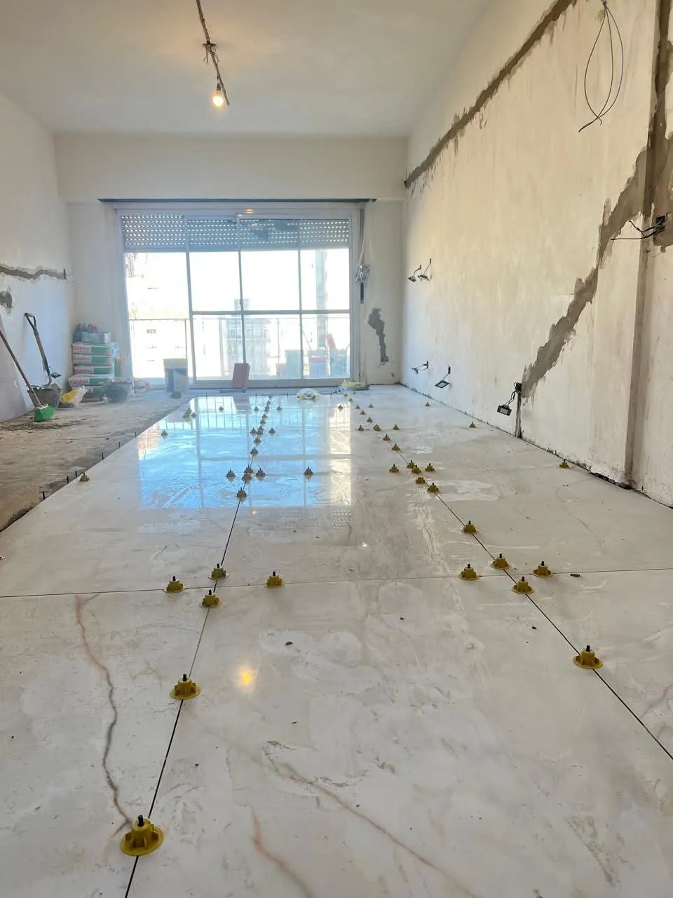 Colocación de piso de porcelanato claro con vetas y niveladores en un ambiente en reforma